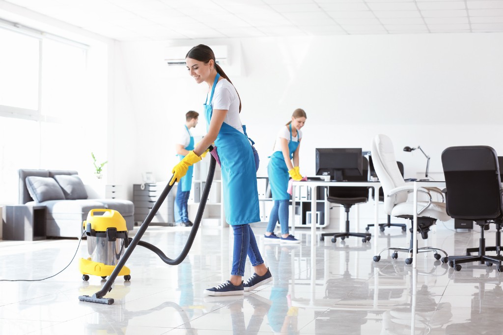Smiling cleaner vacuuming a polished tile floor in a bright modern office