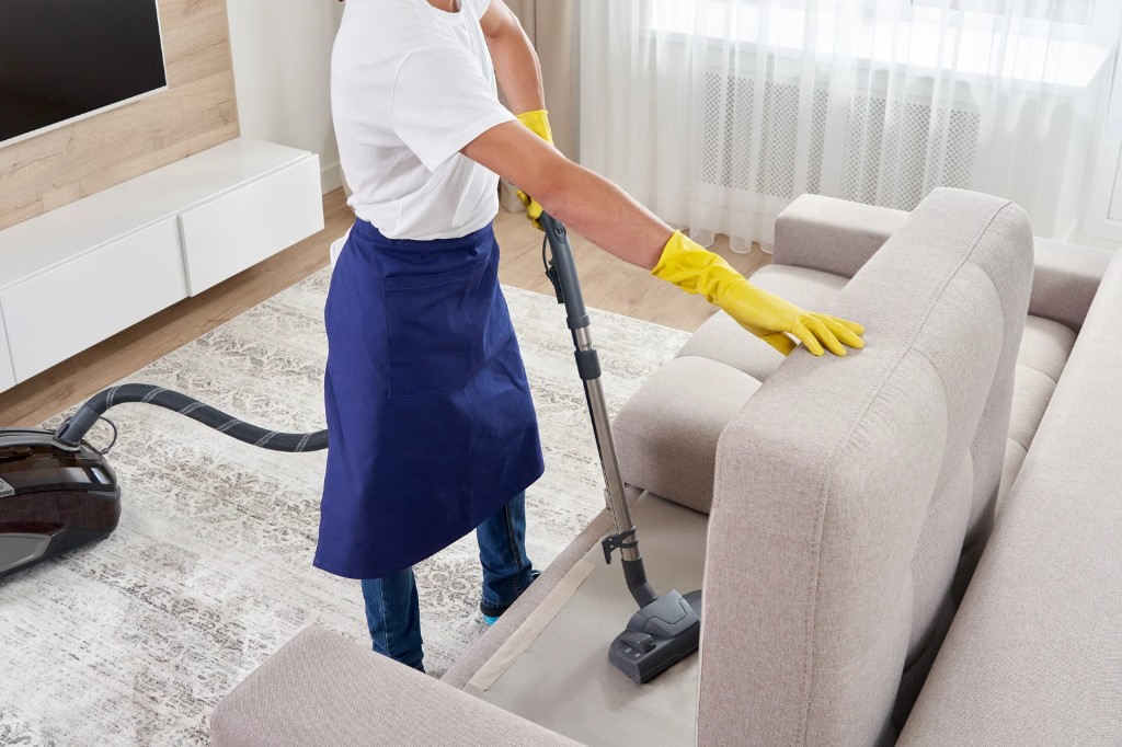 Cleaner vacuuming a fabric sofa with an upholstery attachment